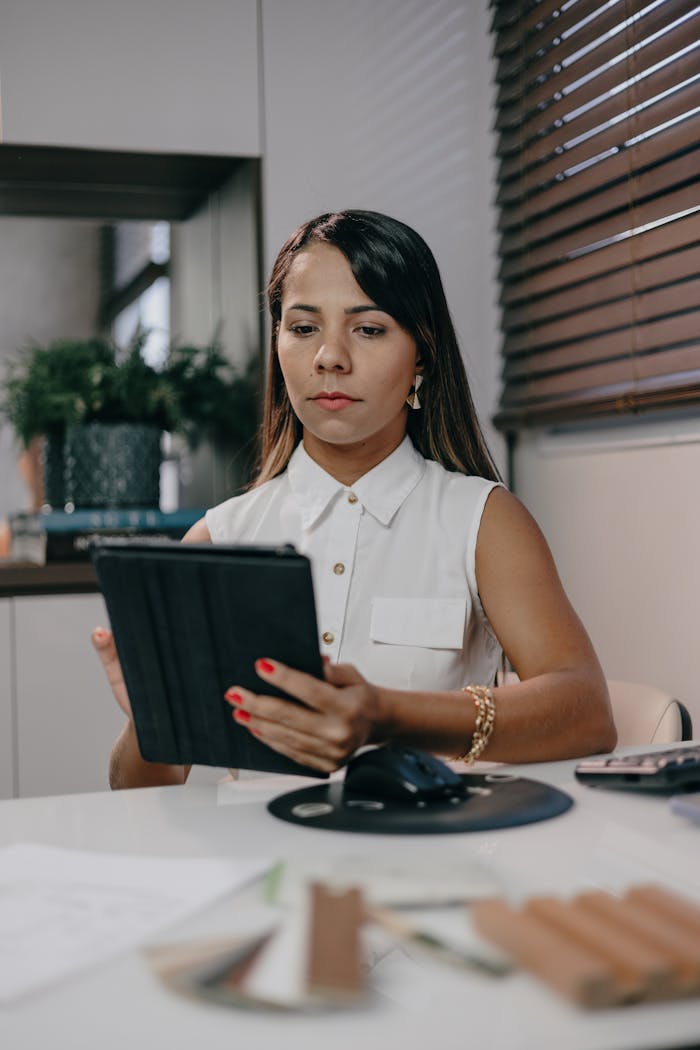 Professional woman in a white shirt using a tablet in a stylish office setting.